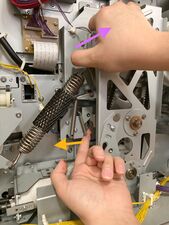 The right hand is lifting up the pressure lever to hold the force of the pressure spring, while the left hand pulls the hook/solenoid lever out to the left.