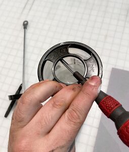 Using leverage from a screwdriver to pop off the black cage on the back of a tube.